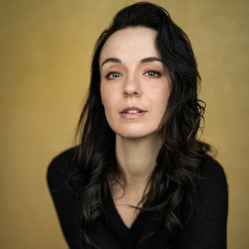 Alice Beaumont, a white woman in her 30s with dark brown hair, wearing a black jumper and blue jeans, leaning towards the camera.