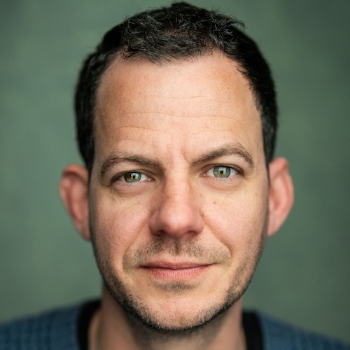 Marc Graham, a white man, black hair, wearing a blue jumper, looking directly at the camera